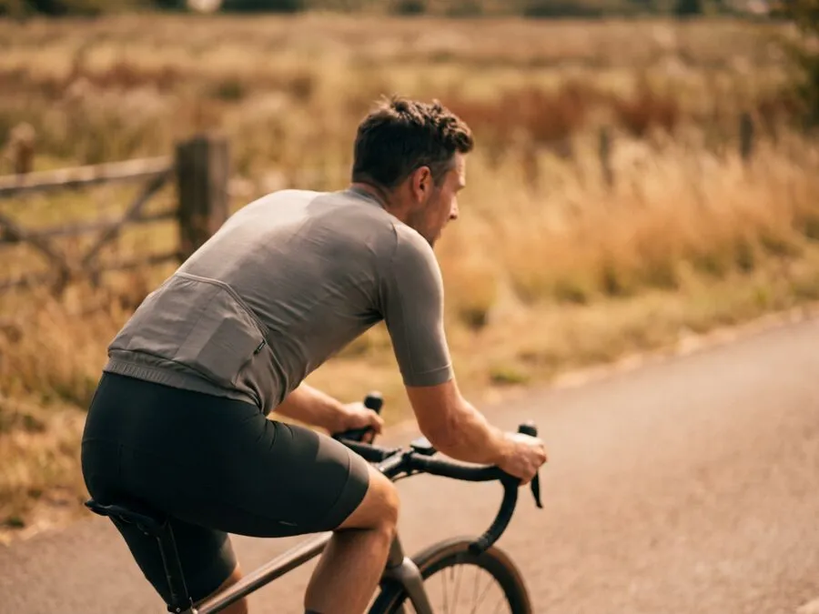A man cycling outdoors on a quiet road, leaning forward over the handlebars in warm natural light