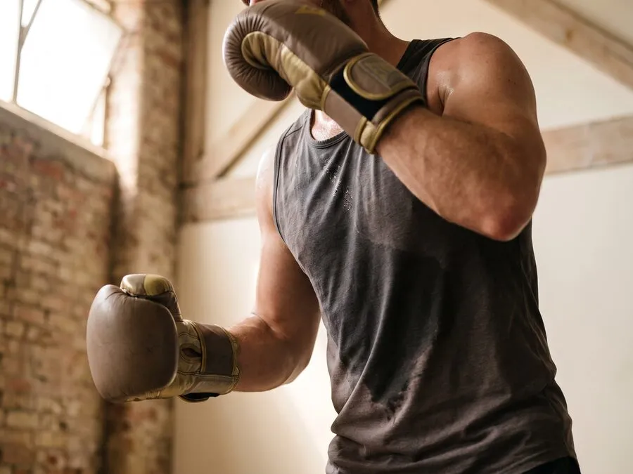 Close view of a man mid-punch in a gym, torso turning into the strike and leather training gloves raised