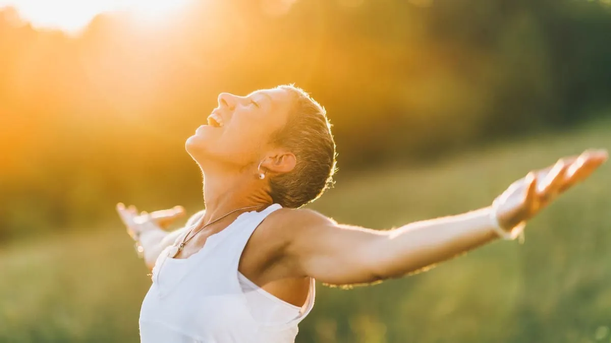 woman in white shirt with arms outstretched in a field