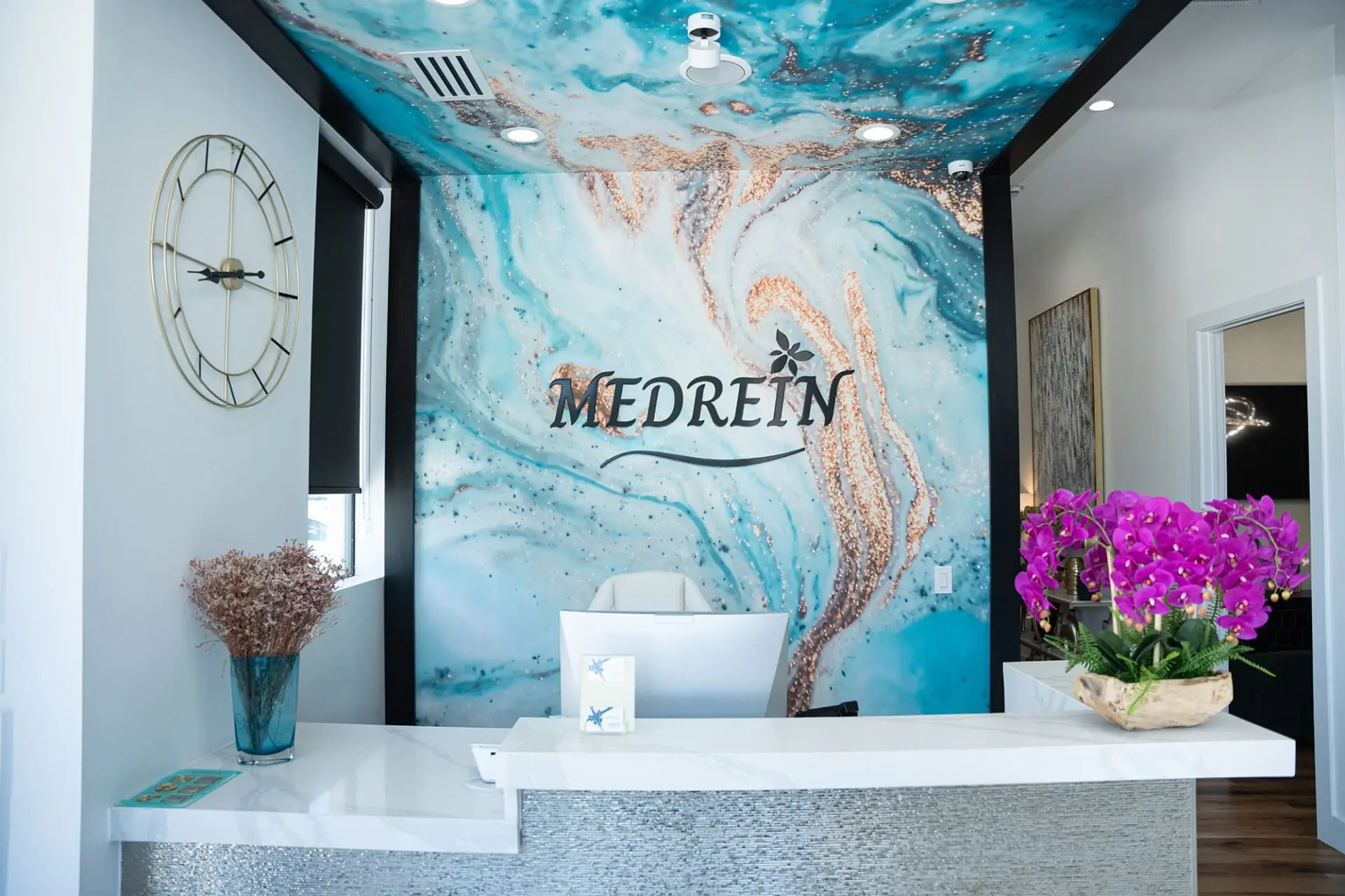 The reception desk at Medrein Health & Aesthetics in Southlake, TX, beneath the practice's teal and copper resin mural