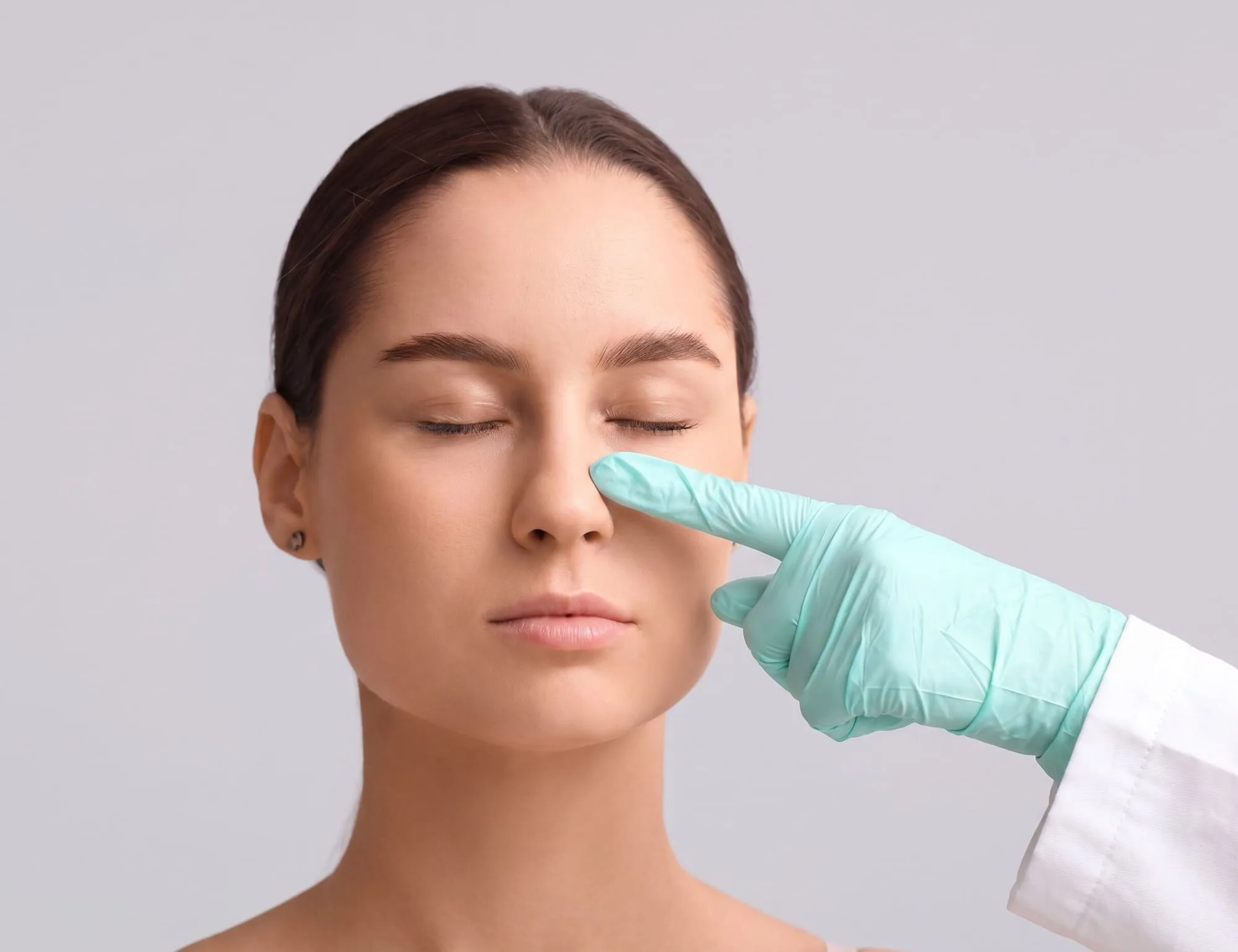 A board-certified physician's gloved fingertip resting at the bridge of a patient's nose during a nose thread lift assessment at Medrein Health in Southlake, TX