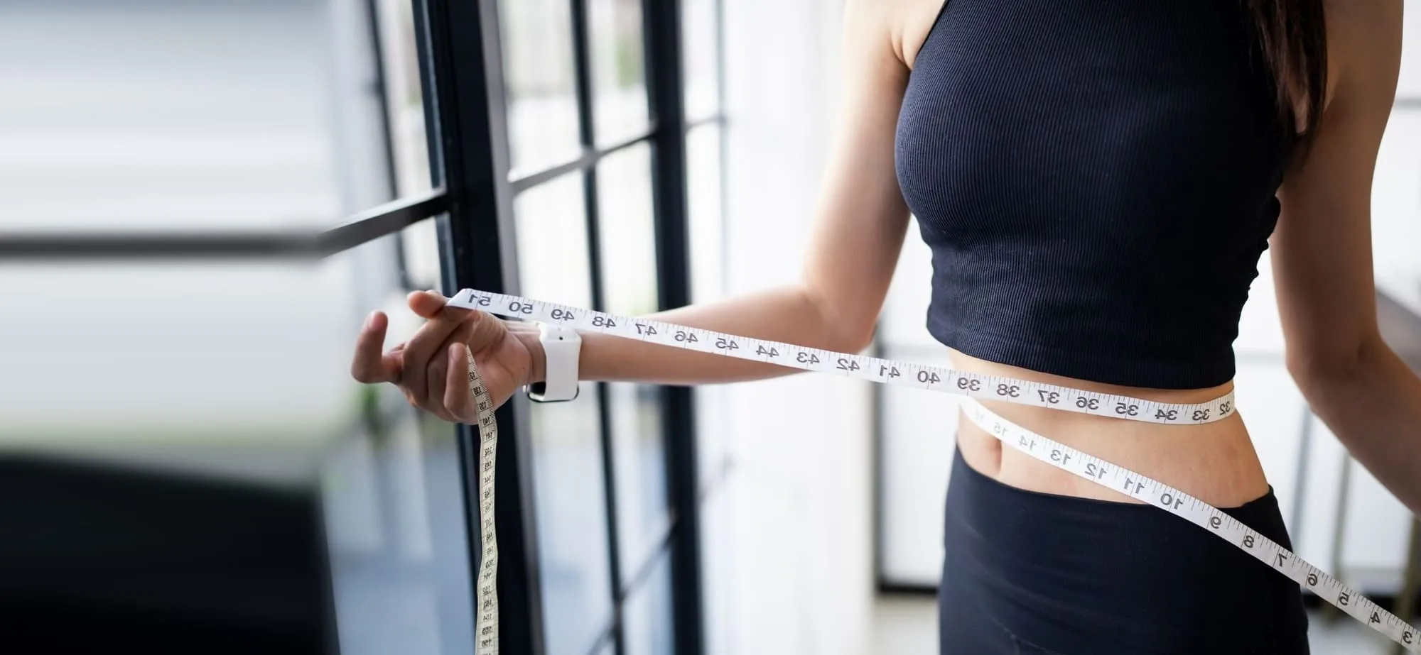 A woman measuring her waist with a tape measure in a bright clinic room