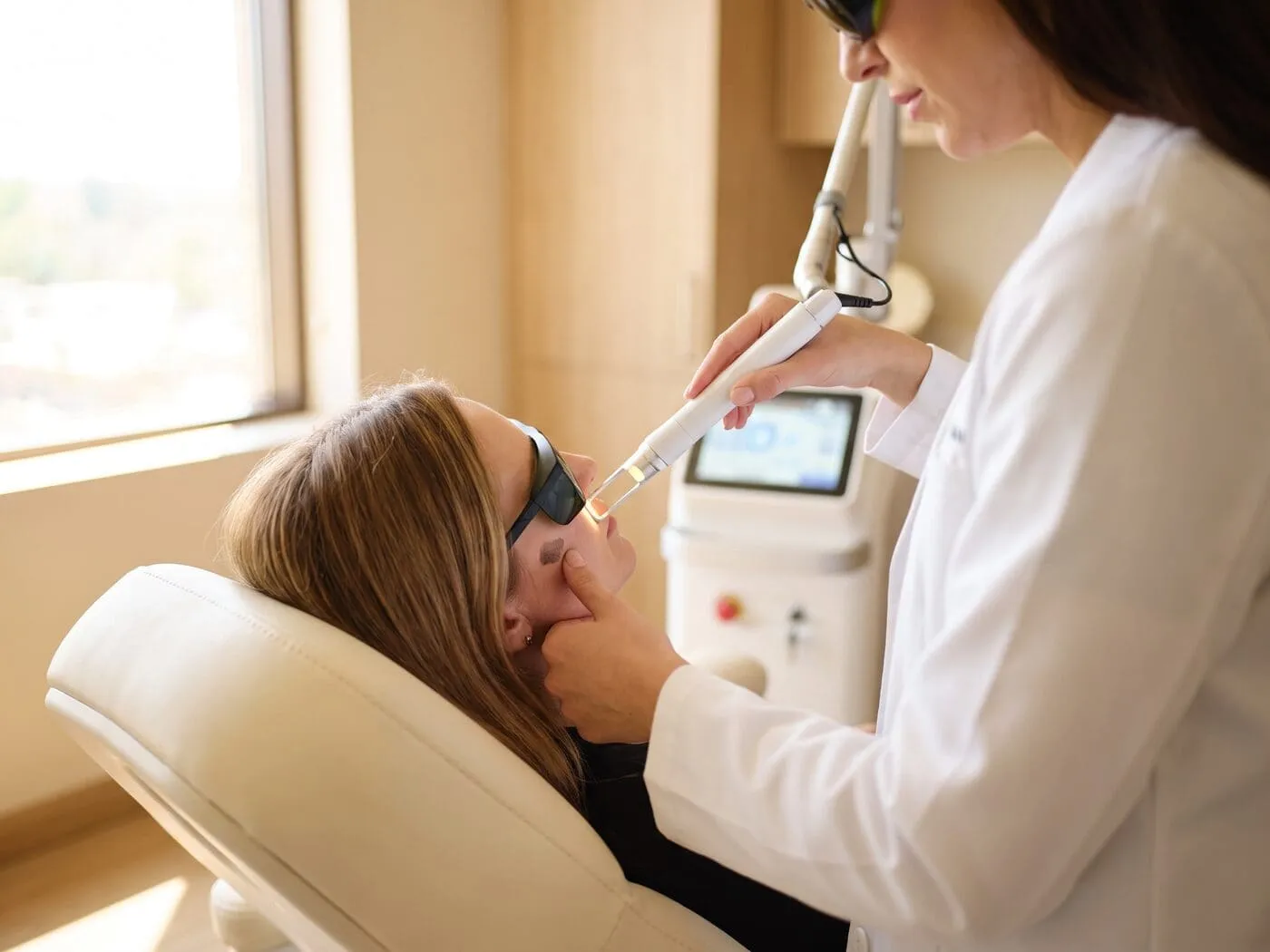 A patient in laser goggles receiving a Picolaser pass over the cheekbone, the StarWalker platform in use beside the chair