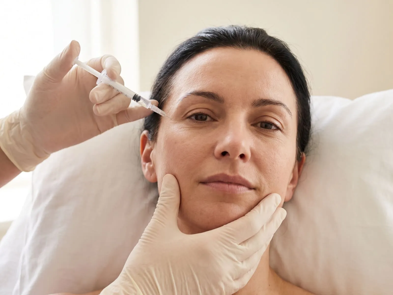 Close view of a gloved clinician placing a collagen biostimulator needle at the temple of a reclining patient