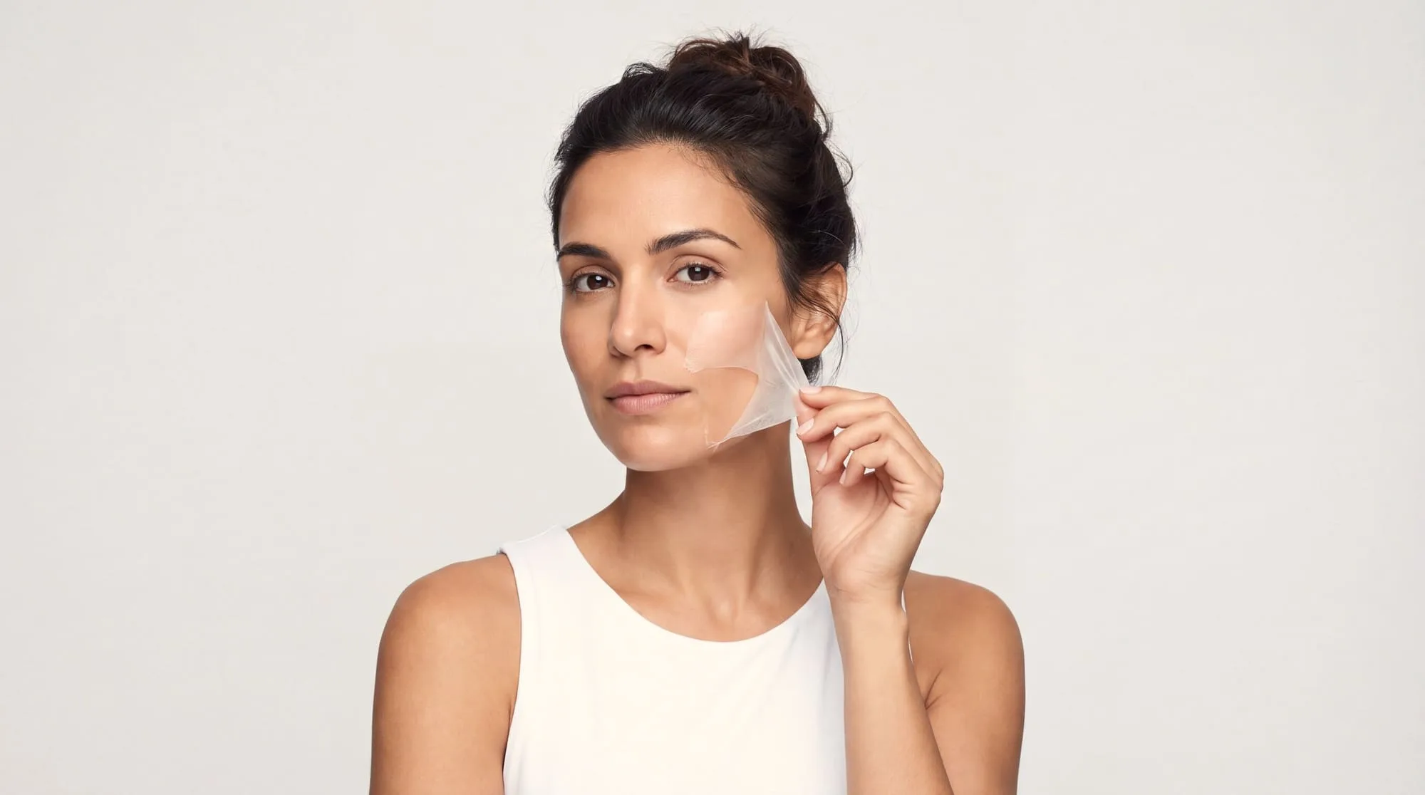 A woman lifting a thin translucent layer of chemical peel away from her cheek after a controlled exfoliation treatment at Medrein Health in Southlake, TX