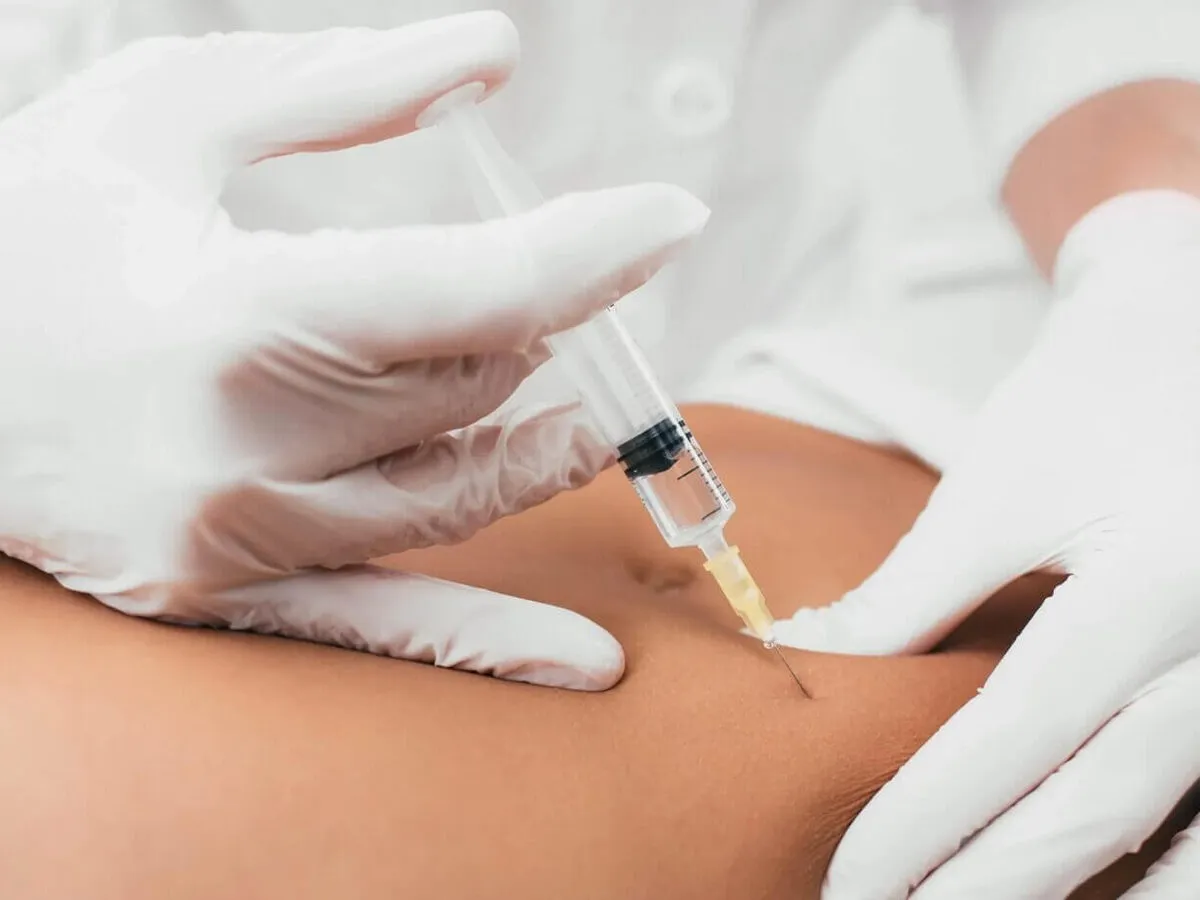 A clinician giving a subcutaneous injection to the abdomen with a fine needle during a weight-loss visit