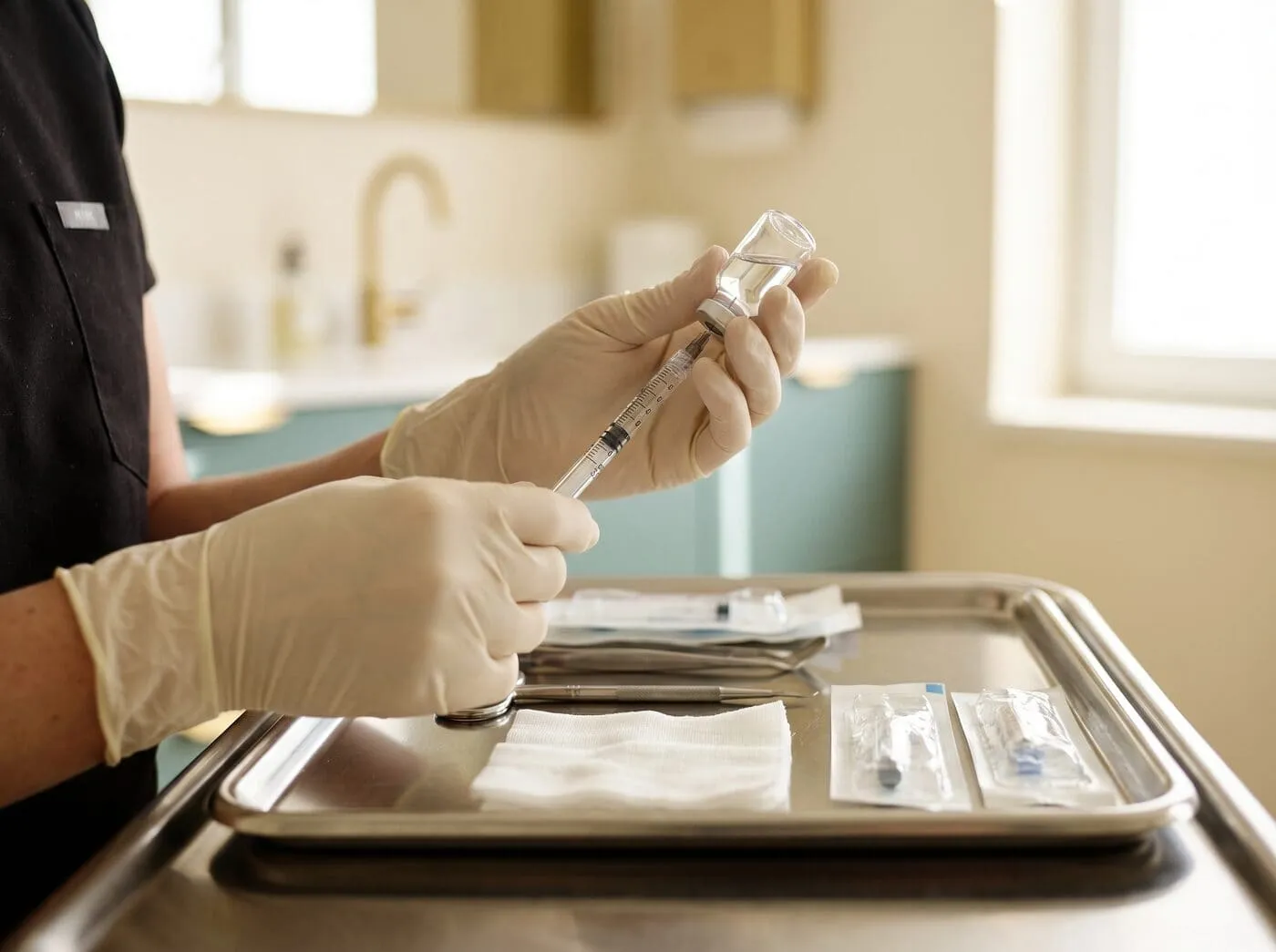 A clinician in gloves preparing a dermal-filler syringe on a sterile tray