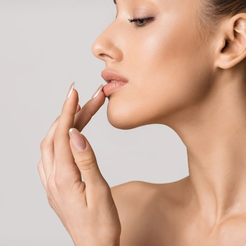 Profile view of a woman resting a fingertip below her lower lip, the natural lip volume and border LipLase builds