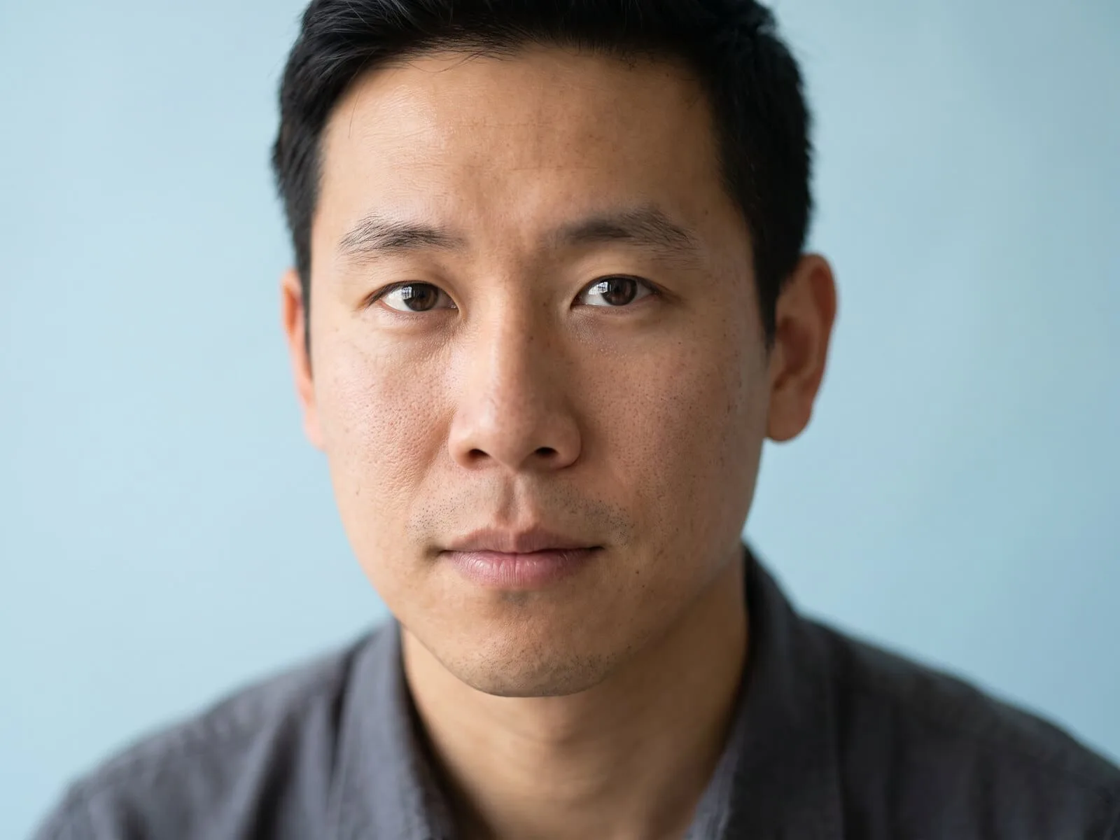 A man in his thirties in close portrait against a pale blue backdrop, looking directly at camera