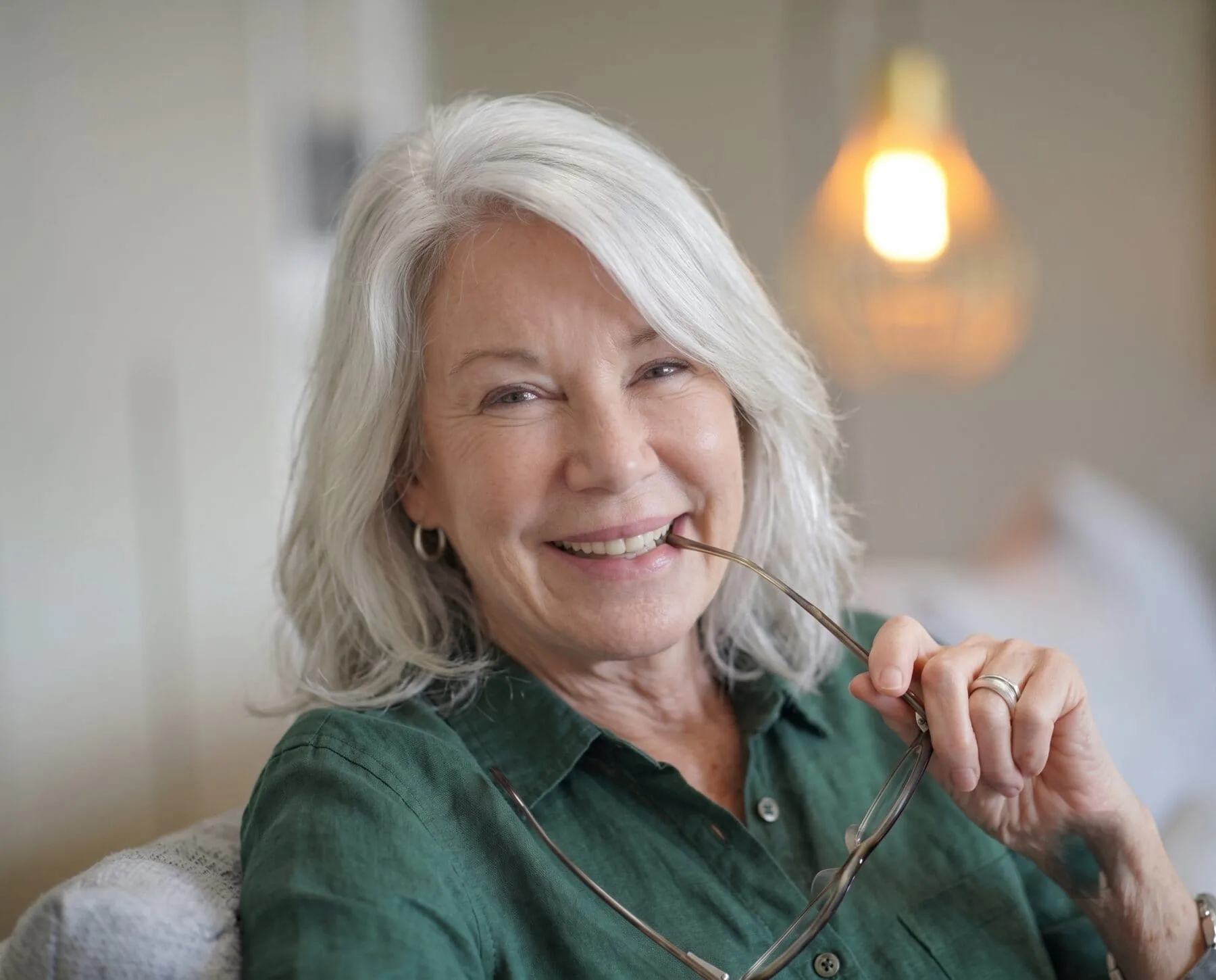 A silver-haired woman in her sixties smiling warmly and holding her glasses, representing the healthy-aging focus of longevity peptide therapy at Medrein Health in Southlake, TX