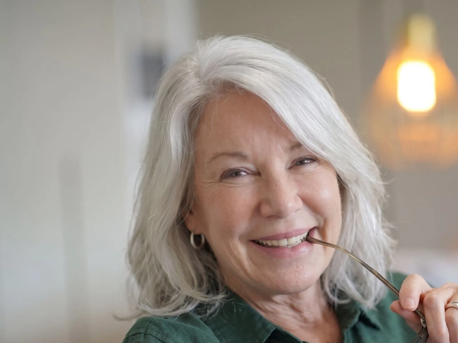 A silver-haired woman in her sixties smiling warmly, holding her glasses